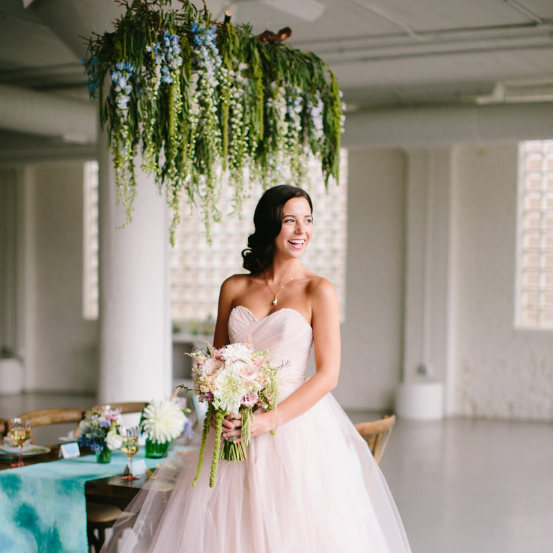 Smiling brunette bride with floral bouquet in front of bridal reception table and floral installation